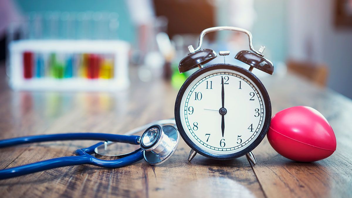 Estetoscopio junto a un reloj despertador y material de laboratorio en una mesa.