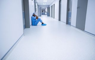 Profesional sanitario sentado en un pasillo vacío del hospital, mostrando ansiedad y agotamiento.