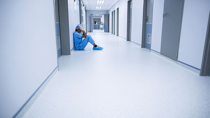 Profesional sanitario sentado en un pasillo vacío del hospital, mostrando ansiedad y agotamiento.